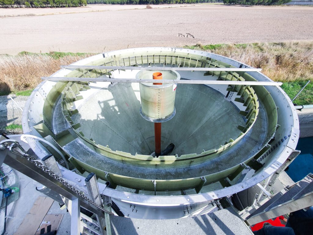 Top-down view of a large, circular industrial component on a construction site with surrounding fields in the background.