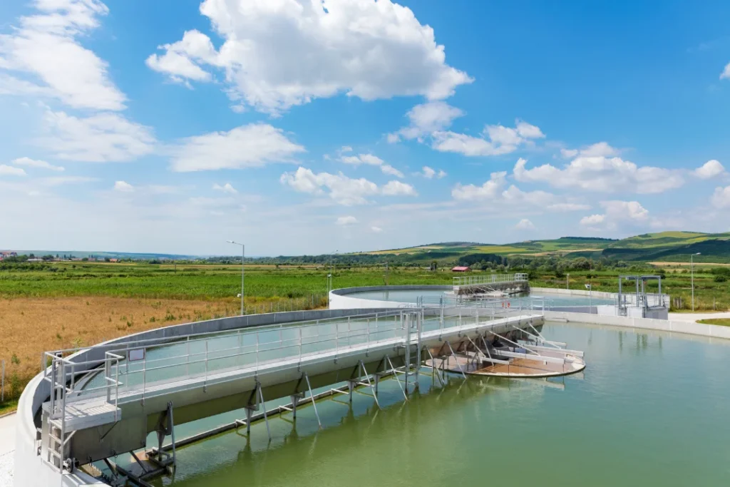 Circular water treatment facility in a rural landscape under a blue sky with clouds.