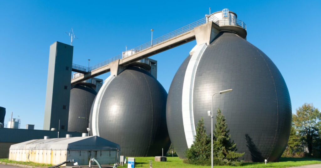 Large, spherical biogas tanks at a wastewater treatment plant on a clear, sunny day with a blue sky background.