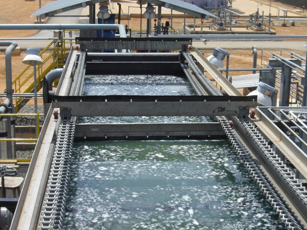Industrial water treatment facility with tanks, filters, and machinery visible, focusing on a large water basin with surface bubbles.