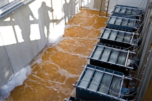 Industrial water treatment facility with flowing brown water and multiple filtration units on the right side of the image.