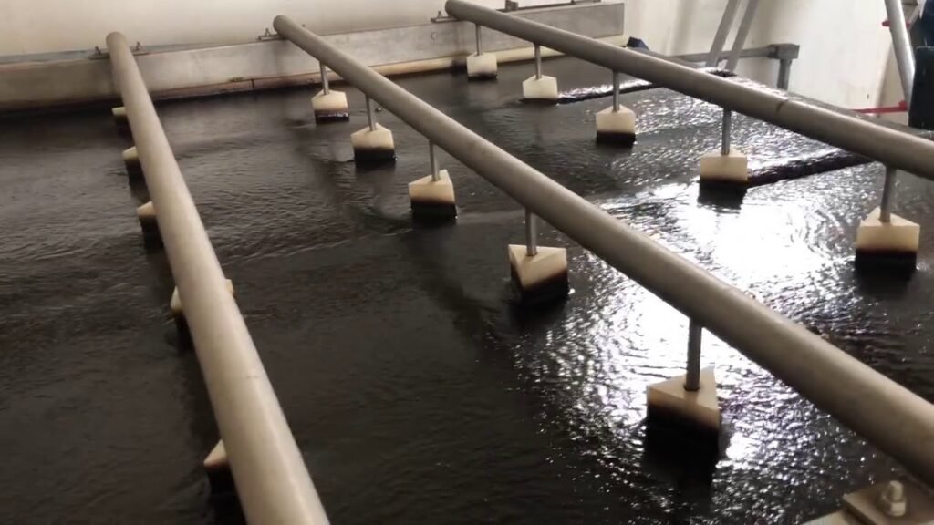 Industrial water filtration system with multiple horizontal pipes and filters in a large tank of water.