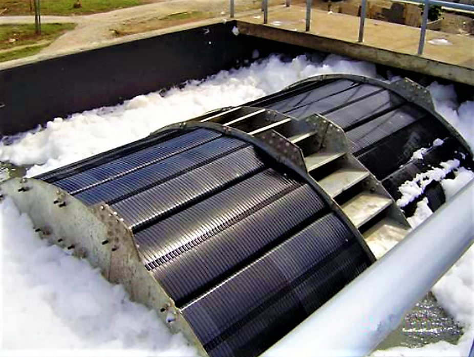 Aeration device with rotating drums in a wastewater treatment plant, surrounded by foam, under a blue sky.