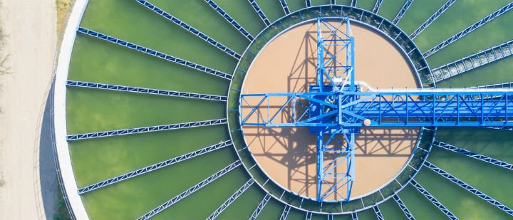 Aerial view of a large circular water treatment facility with blue steel beams and green and brown sections.