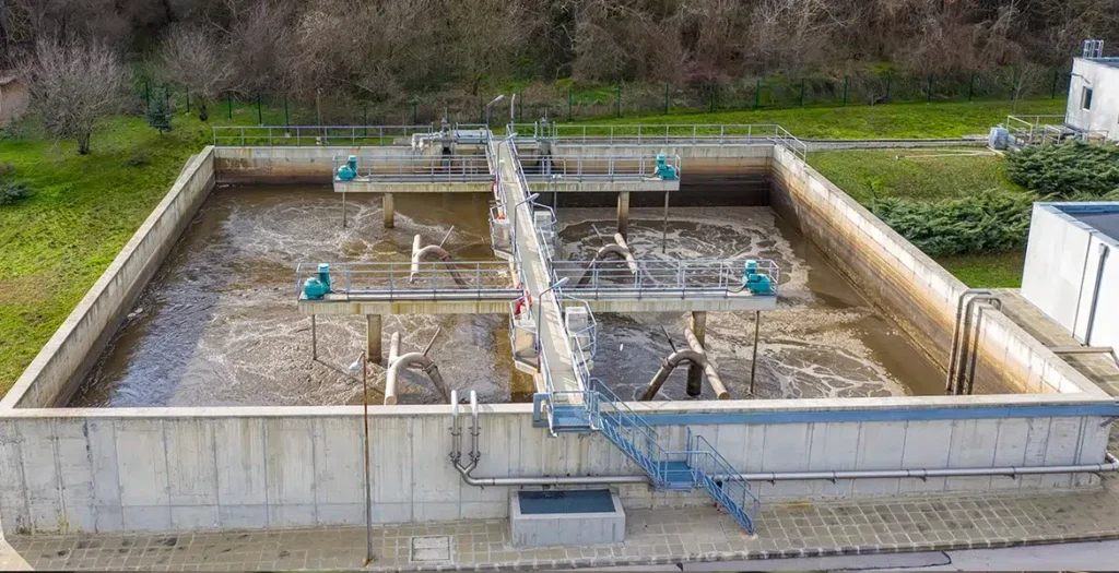 Aerial view of a wastewater treatment facility with aeration tanks and equipment, surrounded by greenery.