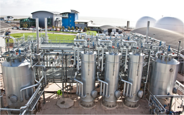 Aerial view of an industrial water treatment plant with large metal tanks and pipes, set near the coast.