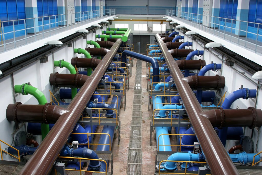 Interior of a water treatment plant with large brown, green, and blue pipes running parallel, viewed from above.