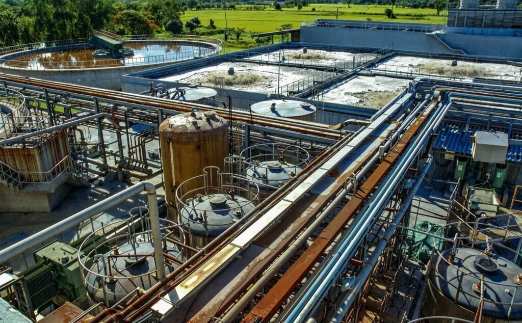 Aerial view of an industrial water treatment facility with various tanks, pipelines, and machinery, surrounded by green fields.