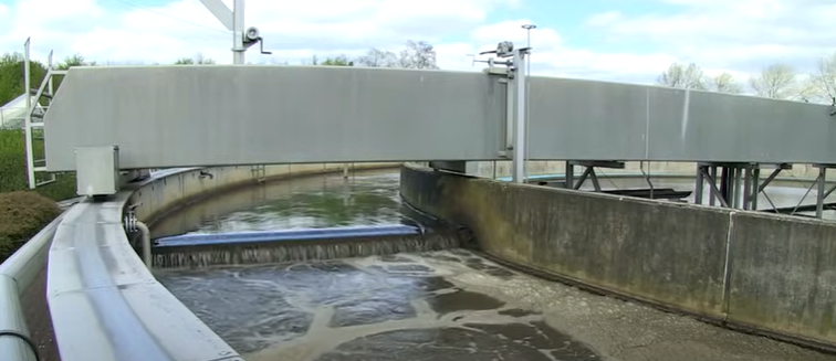 Large circular tank of a wastewater treatment plant with water flowing over the weir inside.