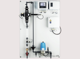 Industrial water treatment panel with gauges, pipes, and electronic controls mounted on a white board.