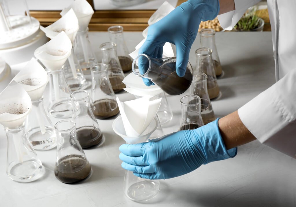 Scientist in blue gloves pouring liquid into a funnel with filter paper, surrounded by Erlenmeyer flasks.