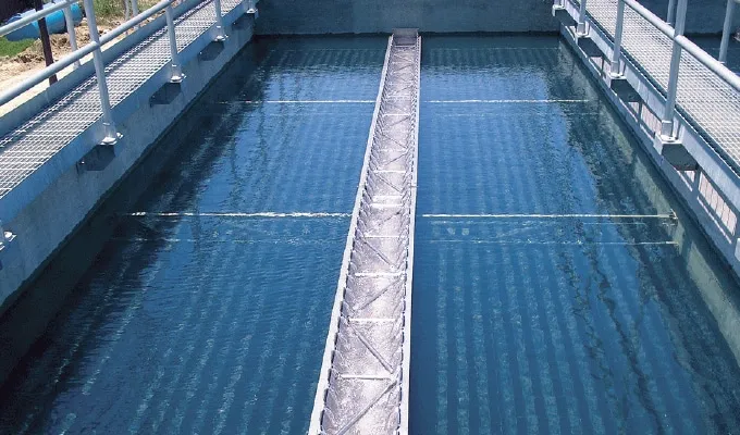 Clear water in a rectangular treatment tank with metal walkways and safety railings on both sides.