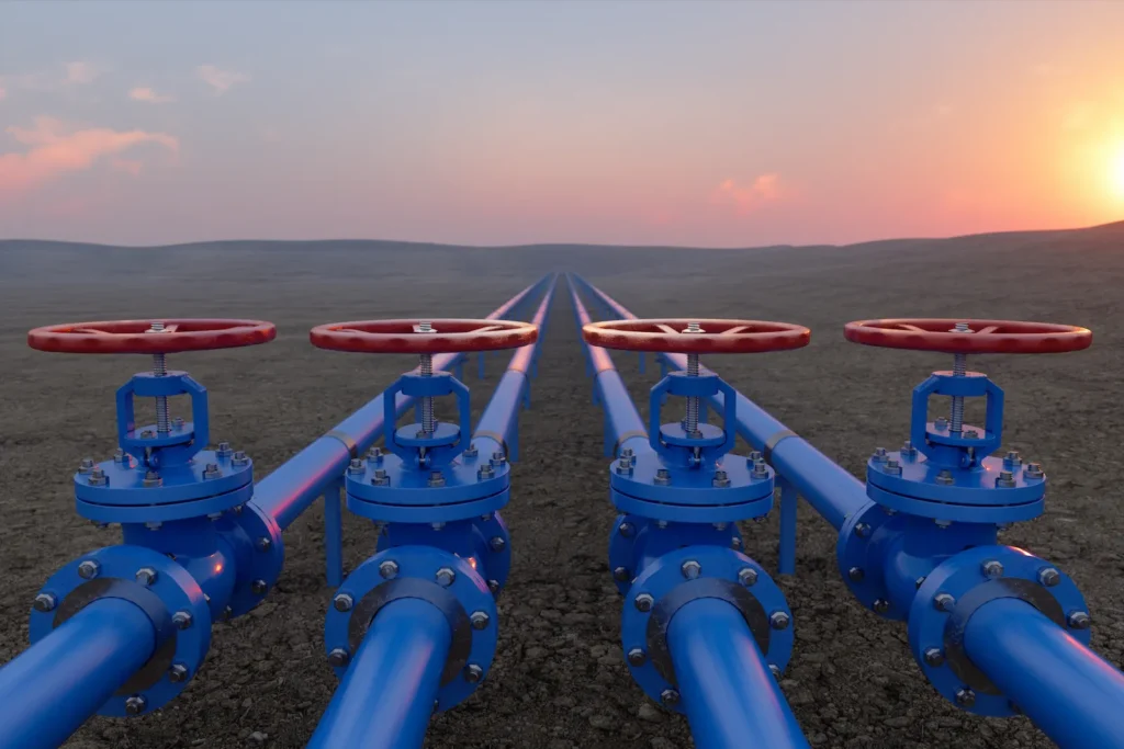 Four blue industrial pipelines with red valves stretch into the distance at sunset.