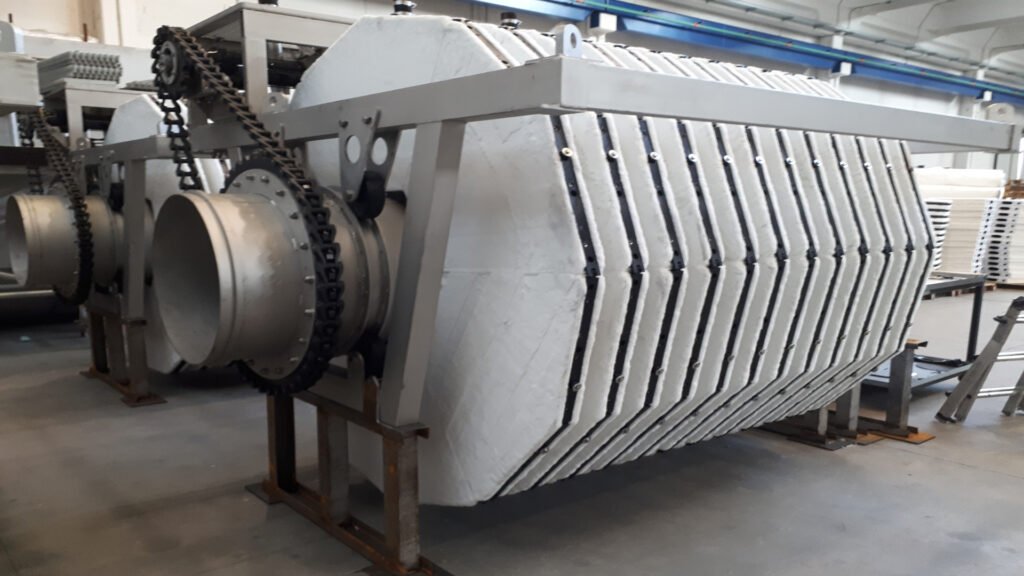 Industrial machinery with a large, segmented metal drum and chain mechanism, situated in a factory setting.