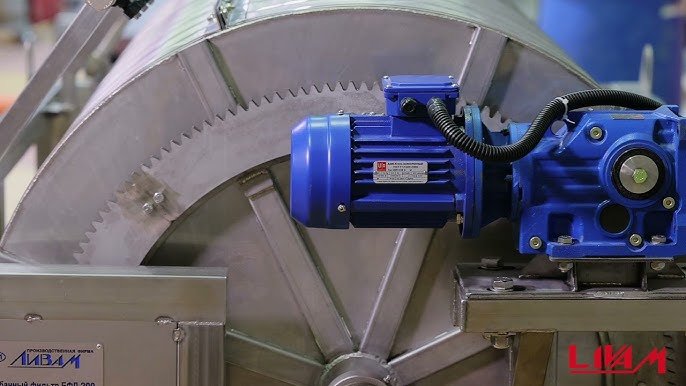 Industrial blue motor attached to a large metal drum with gear teeth, featuring a manufacturer's label, placed in a machinery setting.