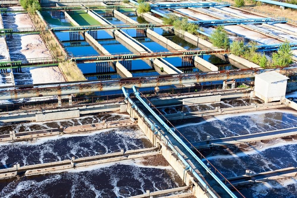 Aerial view of a wastewater treatment plant with multiple rectangular tanks and greenery around.