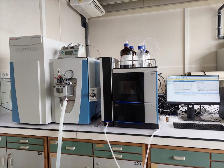 Laboratory setup with mass spectrometer, liquid chromatography system, and computer on a bench for chemical analysis.