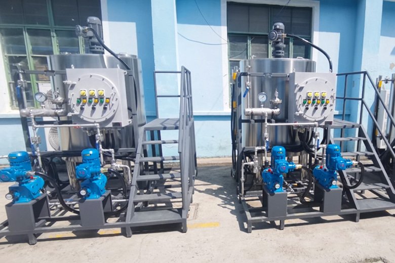 Two industrial stainless steel machines with blue pumps and control panels outside a blue building.