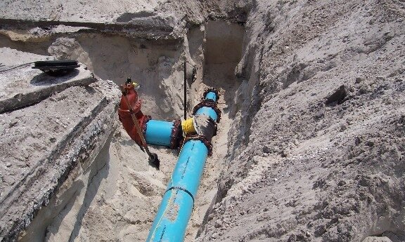 Blue water pipes in a trench surrounded by sand, showing excavation and installation process.
