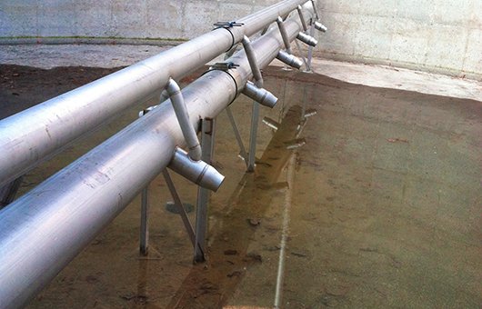 Industrial pipes in a concrete basin with shallow water, featuring angled nozzles and support structures.