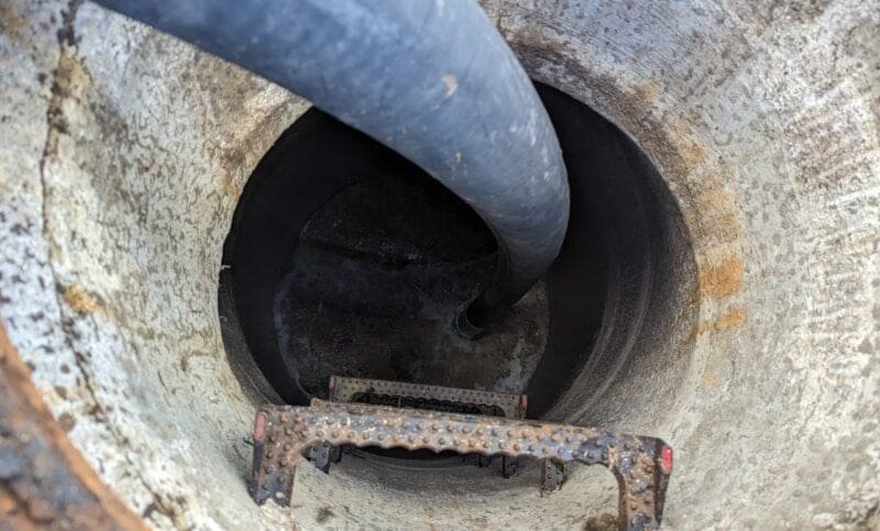 View inside a concrete well with a large black pipe and rusted metal ladder steps.