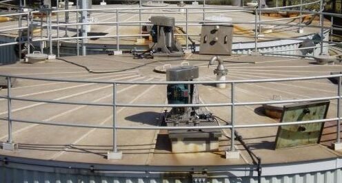 Industrial water treatment tank with metal railings and machinery on top, located in an outdoor setting.