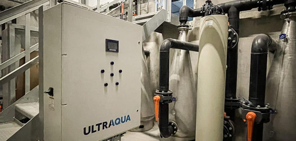 Industrial water treatment system with ULTRAQUA control panel and large pipes in a facility.