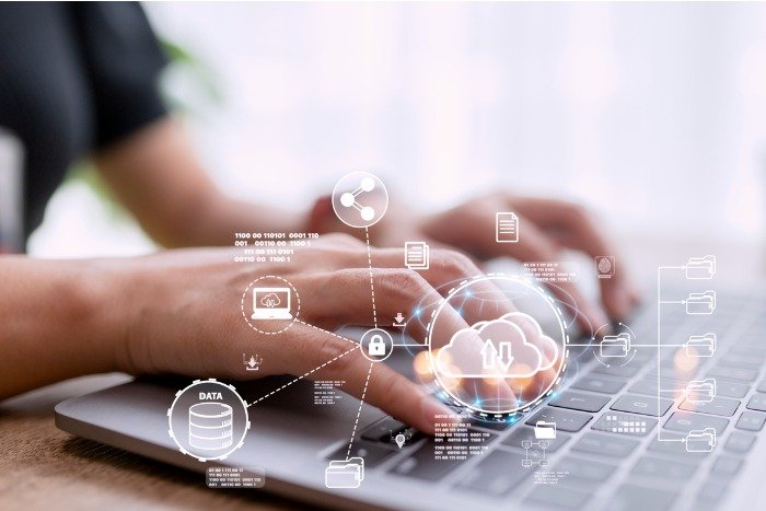 Hands typing on laptop with holographic cloud computing icons, representing data storage and security concepts.